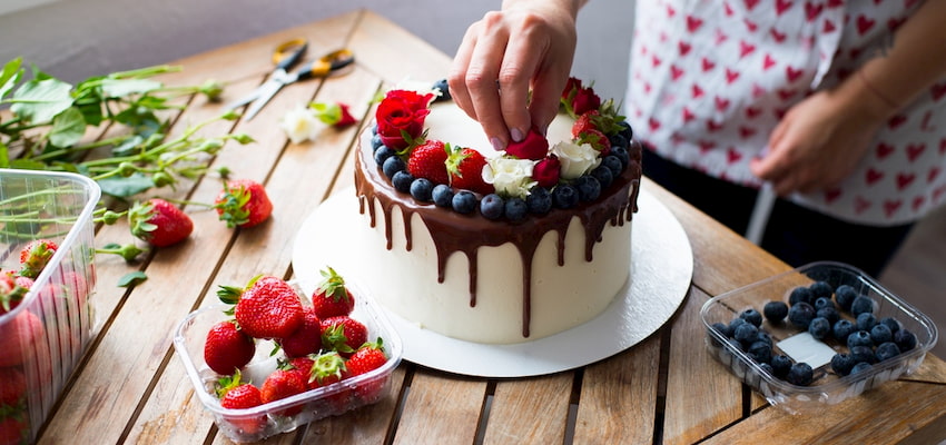a woman decorates a cake with fruit and chocolate