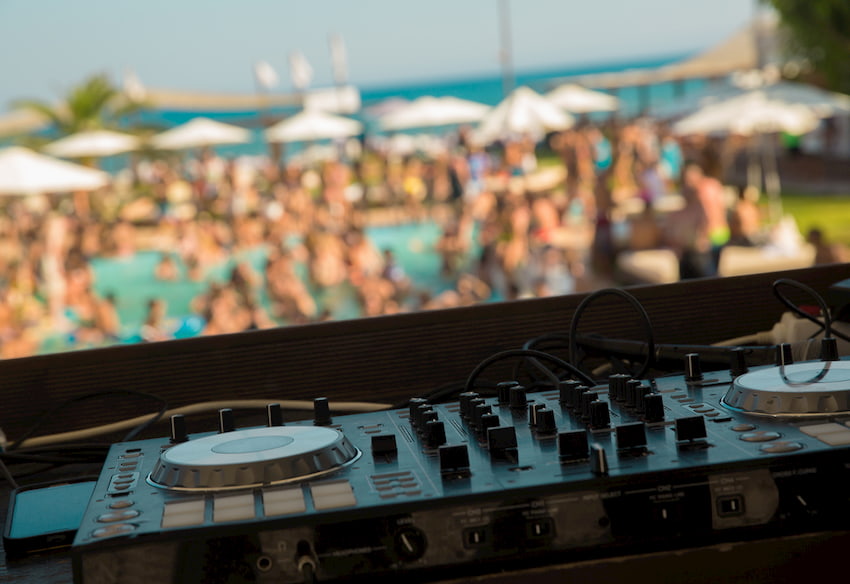 a DJ booth leads a pool party while attendees dance near the water