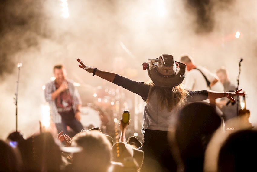 girl wearing a cowboy hat cheers on a country music performer at Stagecoach Festival