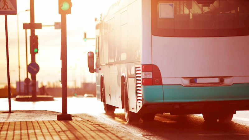 a charter bus drives along a Pasadena street at sunset