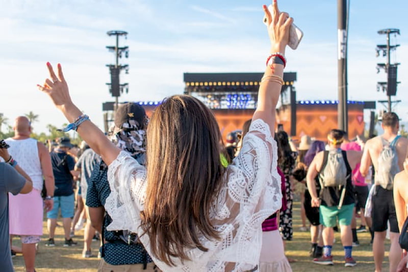 a girl holds up her arms during an exciting concert outdoors at coachella