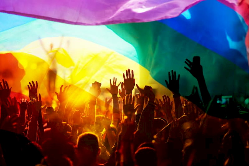 friends hold up their hands during a concert at LA Pride. a rainbow flag waves in the foreground