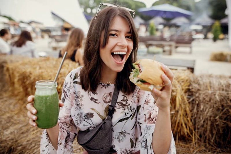 a girl smiles and holds up a plant-based burger at los angeles's vegfest