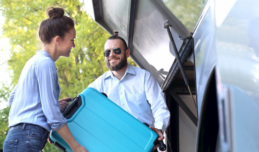 a charter bus driver helps a passenger load luggage into a luggage bay in Los Angeles California