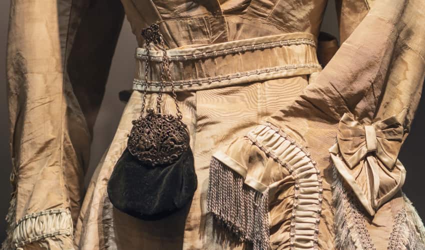 a century-old-dress and purse rest on a mannequin in a museum