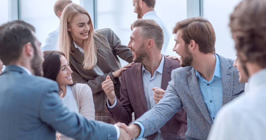 A group of colleagues smiling as two men shake hands