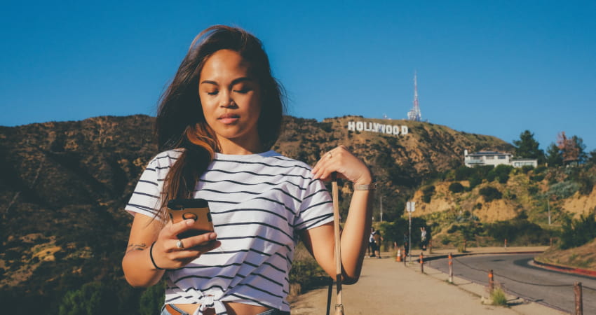 A woman texts on her phone with the Hollywood sign in the background