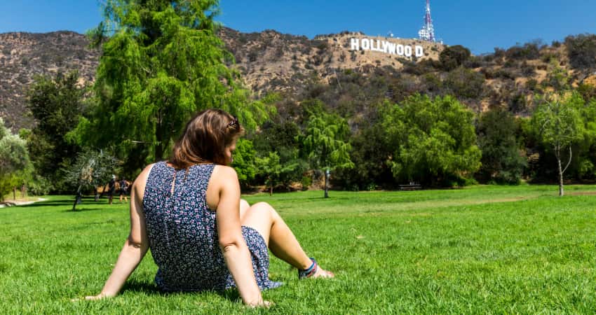 A woman sits on the grass in a park underneath the Hollywood sign