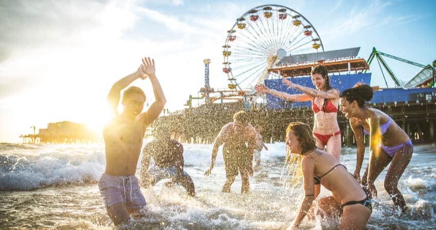 A group of people splashing in the water on the beach with the Santa Monica Pier in the background