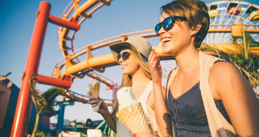 Two people enjoying ice cream on the pier in front of a rollercoaster