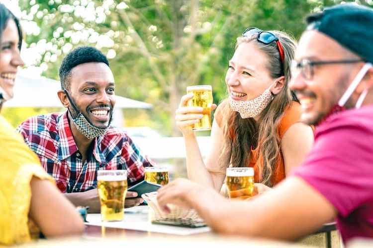 Friends drinking outside with face masks lowered