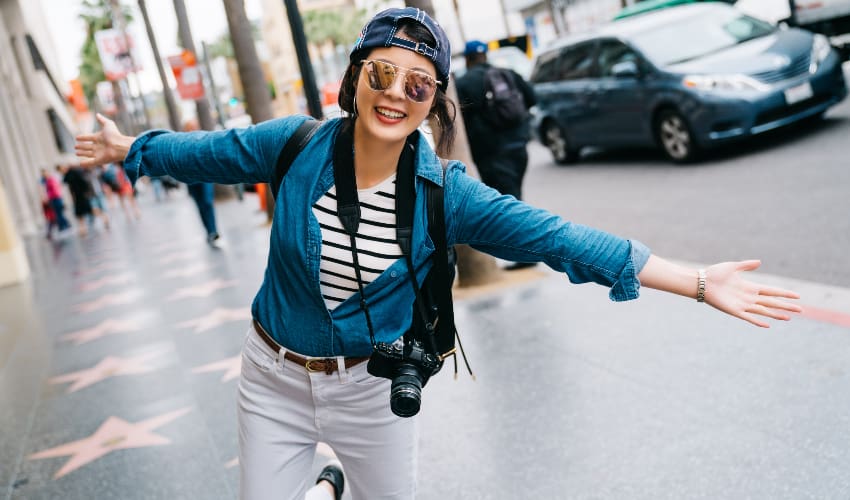 A tourist with a camera poses and smiles on the Hollywood Walk of Fame