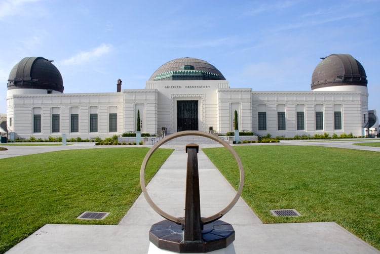 the exterior lawn of griffith observatory with a sculpture pointing to the entrance