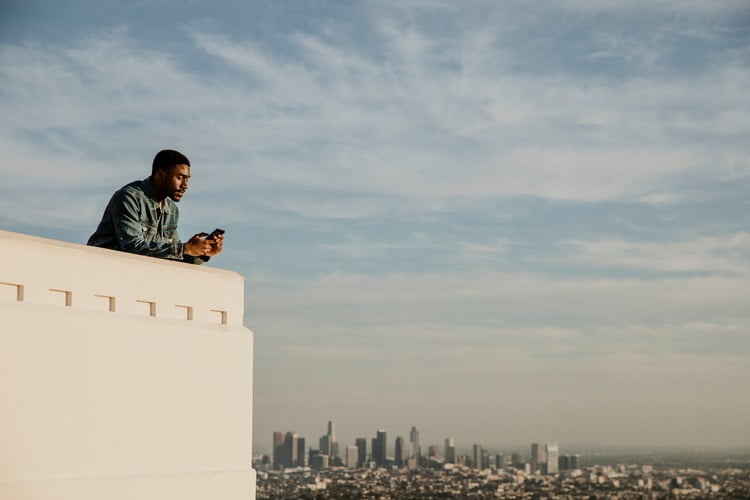 a man leans on the edge of a high observatory point and looks at his phone