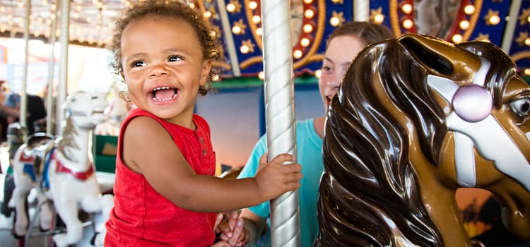 a child smiles while sitting on a horse on a carousel