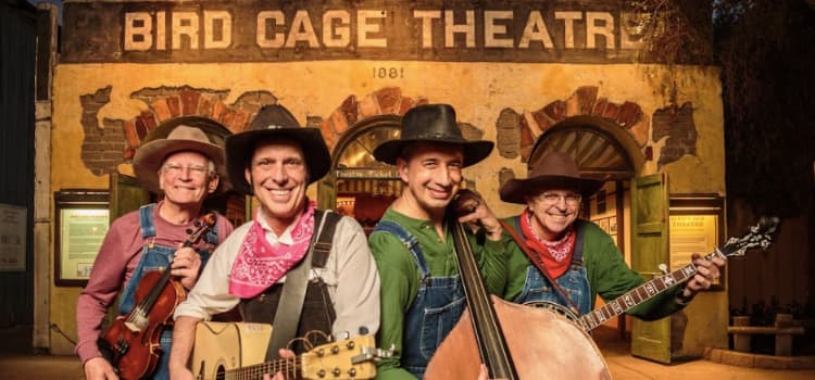 a band dressed in cowboy hats and overalls holds their instruments in front of a stage with a sign that reads "bird cage theatre"
