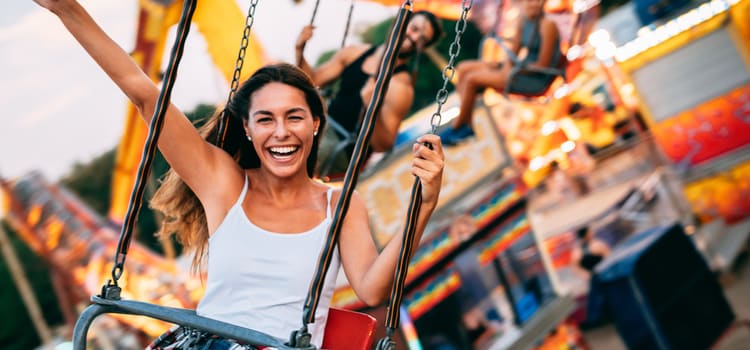 woman smiles and holds up her arm while riding on a chairswing above a theme park