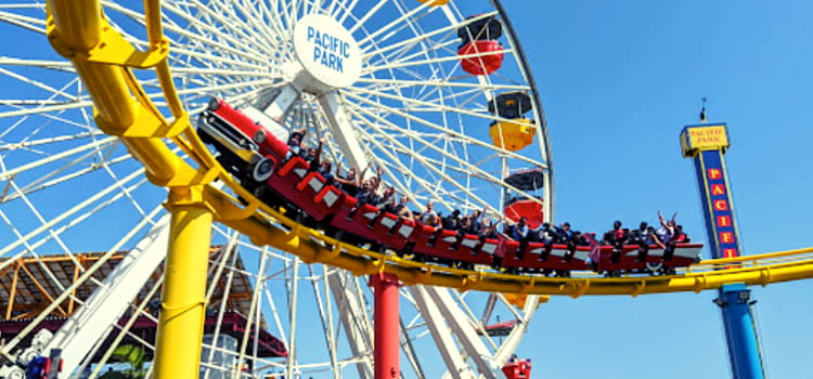 a rollercoaster roars through a turn with a ferris wheel in the background