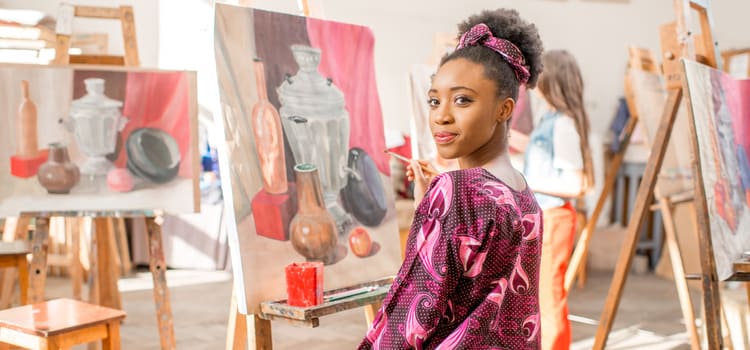 a woman looks over her shoulder as she works on a painting