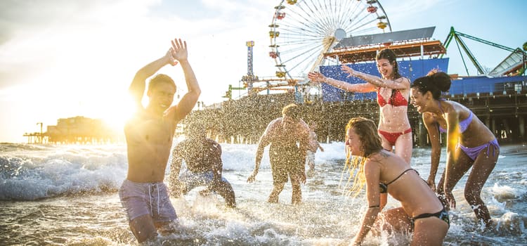 friends in the water at a beach smile and splash, with a ferris wheel in the background