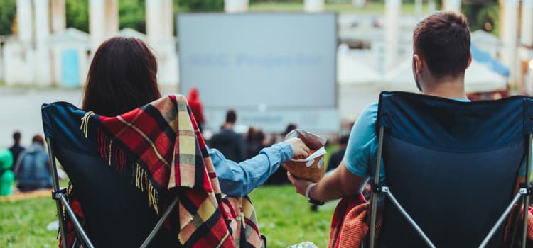 a couple sit in lawn chairs and hold hands while looking at a large projector screen